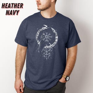 K&ouml;nnte beinhalten: Marineblaues meliertes T-Shirt mit wei&szlig;em Grafikdesign. Das Design zeigt ein kreisf&ouml;rmiges Emblem mit einem kompassartigen Symbol in der Mitte, einen Raben und Runentext. Die Worte "HEATHER NAVY" sind oben links aufgedruckt.