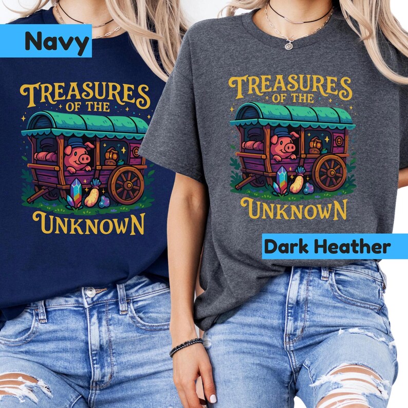 May include: Navy and dark heather t-shirts featuring a whimsical illustration. The design includes a pig in a wagon with the text "Treasures of the Unknown" in gold lettering. The wagon is purple and green, with colorful gems.