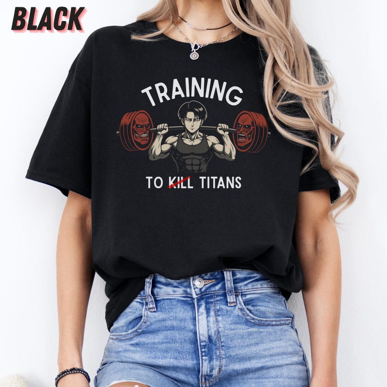 K&ouml;nnte beinhalten: Schwarzes T-Shirt mit dem wei&szlig;en Text "TRAINING TO KILL TITANS". Die Grafik zeigt eine muskul&ouml;se Figur, die eine Langhantel mit zwei rotgesichtigen Titanen an jedem Ende hebt. Das Wort "BLACK" steht oben links.