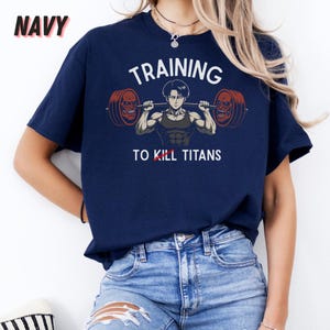 K&ouml;nnte beinhalten: Marineblaues T-Shirt mit dem Wort "NAVY" in der oberen linken Ecke. Das Shirt zeigt eine Grafik eines muskul&ouml;sen Anime-Charakters, der eine Langhantel hebt, mit den Worten "TRAINING TO KILL TITANS" in Wei&szlig;.