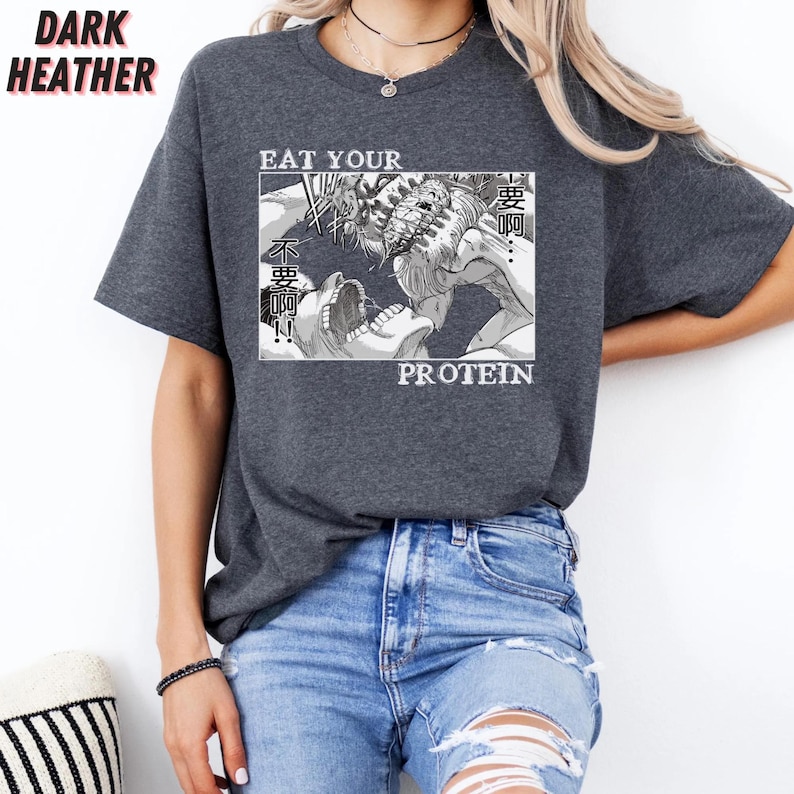 May include: Dark heather gray t-shirt with a manga-style graphic. The graphic features a black and white illustration of a battle scene with the words "EAT YOUR PROTEIN" in white text. The shirt has short sleeves and a crew neck.