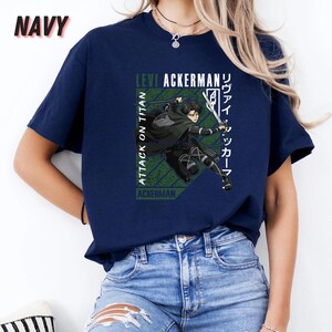 May include: Navy blue t-shirt featuring a graphic of Levi Ackerman from Attack on Titan. The design includes text in English and Japanese, with a green and white color scheme. The shirt is a short-sleeved crew neck.