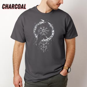 K&ouml;nnte beinhalten: Anthrazitfarbenes T-Shirt mit einer wei&szlig;en Grafik eines Raben, einem kreisf&ouml;rmigen Design mit Runen und anderen Symbolen. Das Wort "CHARCOAL" ist oben in Wei&szlig; aufgedruckt. Das Shirt hat kurze &Auml;rmel.