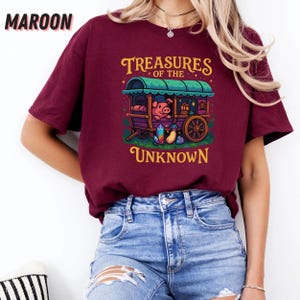 May include: Maroon t-shirt with the text "Treasures of the Unknown." The graphic features a pig in a wagon with colorful gems. The shirt is a short-sleeved crew neck.