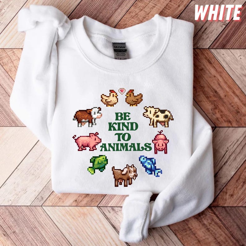 May include: White crewneck sweatshirt with a pixelated animal design. The design includes chickens, cows, pigs, fish, goats, and a pig-shaped fire hydrant. The text "BE KIND TO ANIMALS" is in green. The word "WHITE" is in the top right corner.