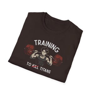 K&ouml;nnte beinhalten: Dunkelbraunes T-Shirt mit einer Grafik eines Anime-Charakters, der Gewichte hebt. Der Text lautet "TRAINING TO KILL TITANS". Die Hantelscheiben haben ein rotes Gesichtsdesign.