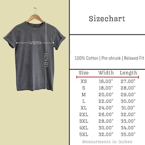 May include: A dark gray t-shirt hanging on a wooden hanger. The image includes a size chart with measurements in inches for sizes XS to 5XL. The shirt is made of 100% cotton, pre-shrunk, and has a relaxed fit.