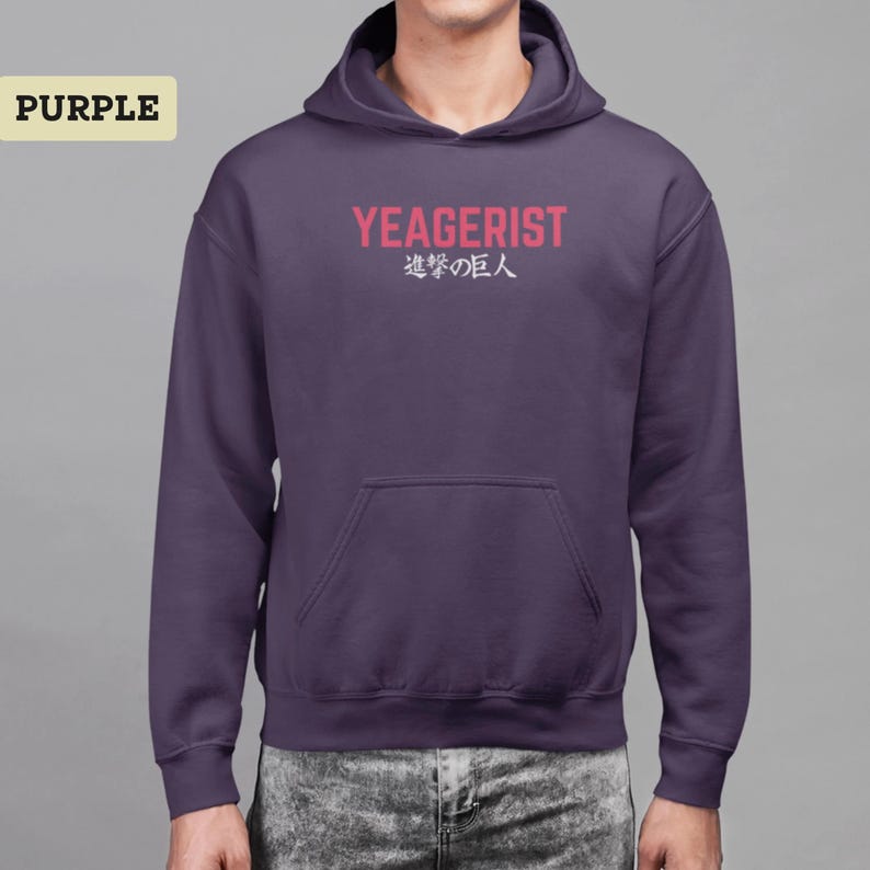 Puede incluir: Una sudadera con capucha de color morado que presenta un bolsillo tipo canguro frontal y el texto YEAGERIST en letras may&uacute;sculas rosas, seguido de los caracteres japoneses 進撃の巨人 en blanco. La sudadera tiene mangas largas.