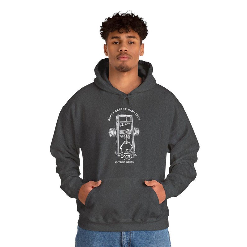 Puede incluir: Sudadera con capucha gris oscuro con bolsillo delantero y cord&oacute;n. El gr&aacute;fico en la parte delantera presenta un esqueleto en una guillotina con las palabras "DEPTH BEFORE DISHONOR" y "CUTTING DEPTH" en un dise&ntilde;o circular.
