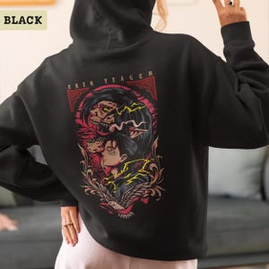 Puede incluir: Una sudadera con capucha negra que presenta un gr&aacute;fico en la parte posterior con el texto EREN YEAGER. El dise&ntilde;o muestra una ilustraci&oacute;n estilizada de un personaje y una figura monstruosa con acentos rojos y amarillos, enmarcada por volutas.