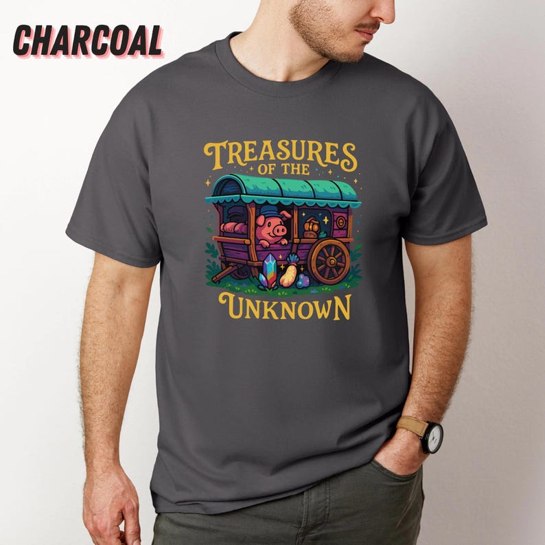 May include: Charcoal gray t-shirt featuring a whimsical illustration. The design includes a pig in a caravan with the text "Treasures of the Unknown". The artwork is in shades of green, purple, yellow, and blue.