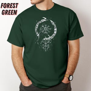 K&ouml;nnte beinhalten: Forstgr&uuml;nes T-Shirt mit wei&szlig;em Grafikdesign. Das Design zeigt einen Raben, eine kreisf&ouml;rmige Rune und andere Symbole. Das Shirt besteht aus einem weichen Material und hat kurze &Auml;rmel.
