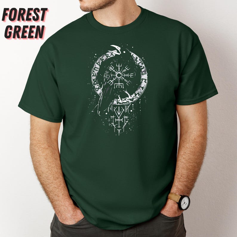 K&ouml;nnte beinhalten: Forstgr&uuml;nes T-Shirt mit wei&szlig;em Grafikdesign. Das Design zeigt einen Raben, eine kreisf&ouml;rmige Rune und andere Symbole. Das Shirt besteht aus einem weichen Material und hat kurze &Auml;rmel.