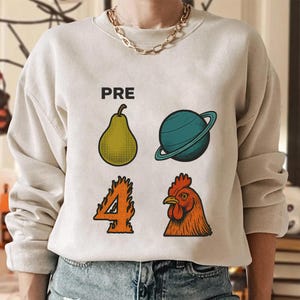 Könnte beinhalten: Beiges Sweatshirt mit dem Wort "PRE" über einer Birne, einem Planeten mit Ringen, der Zahl 4 in Flammen und einem Hahn. Das Design ist im Cartoon-Stil mit schwarzen Umrissen und leuchtenden Farben gehalten.