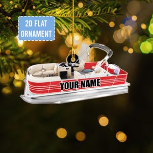 May include: A 2D flat ornament shaped like a red and white pontoon boat. The boat has beige seating, a black steering wheel, and the text "YOUR NAME" in black. The ornament is hanging from a gold string.