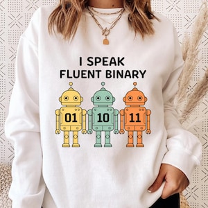 Op de afbeelding: Witte sweatshirt met de tekst "I Speak Fluent Binary" en drie robotillustraties. De robots zijn geel, blauwgroen en oranje, elk met een binair getal: 01, 10 en 11.
