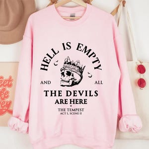 May include: A pale pink sweatshirt featuring the phrase "HELL IS EMPTY AND ALL THE DEVILS ARE HERE" and a skull wearing a crown. The text also includes "THE TEMPEST ACT I, SCENE II".
