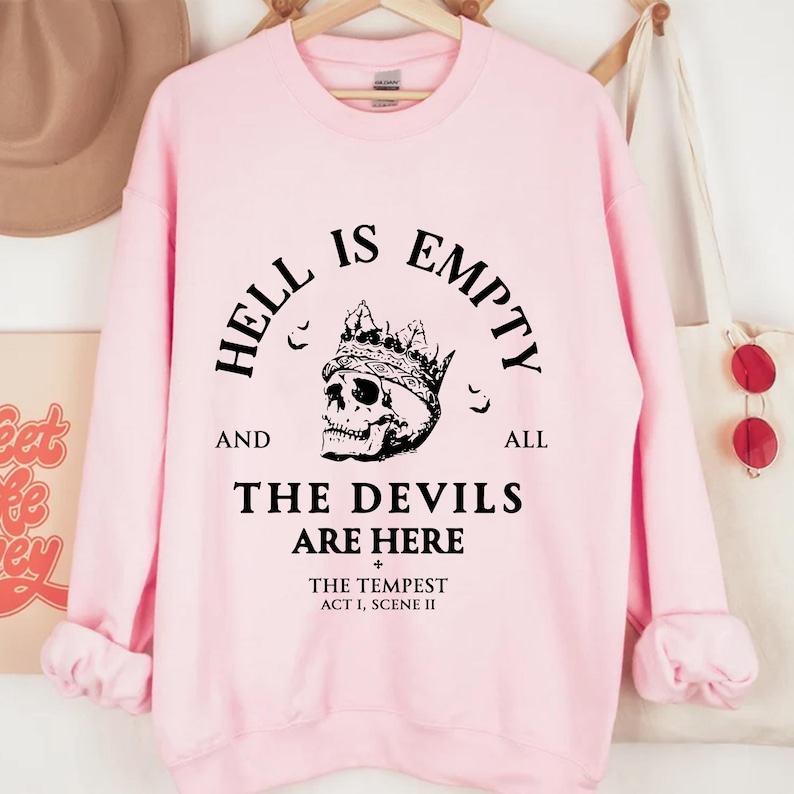 May include: A pale pink sweatshirt featuring the phrase "HELL IS EMPTY AND ALL THE DEVILS ARE HERE" and a skull wearing a crown. The text also includes "THE TEMPEST ACT I, SCENE II".