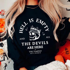 May include: Black sweatshirt featuring the quote "HELL IS EMPTY AND ALL THE DEVILS ARE HERE" with a skull wearing a crown. The text also includes "THE TEMPEST ACT I, SCENE II". The design is in white.