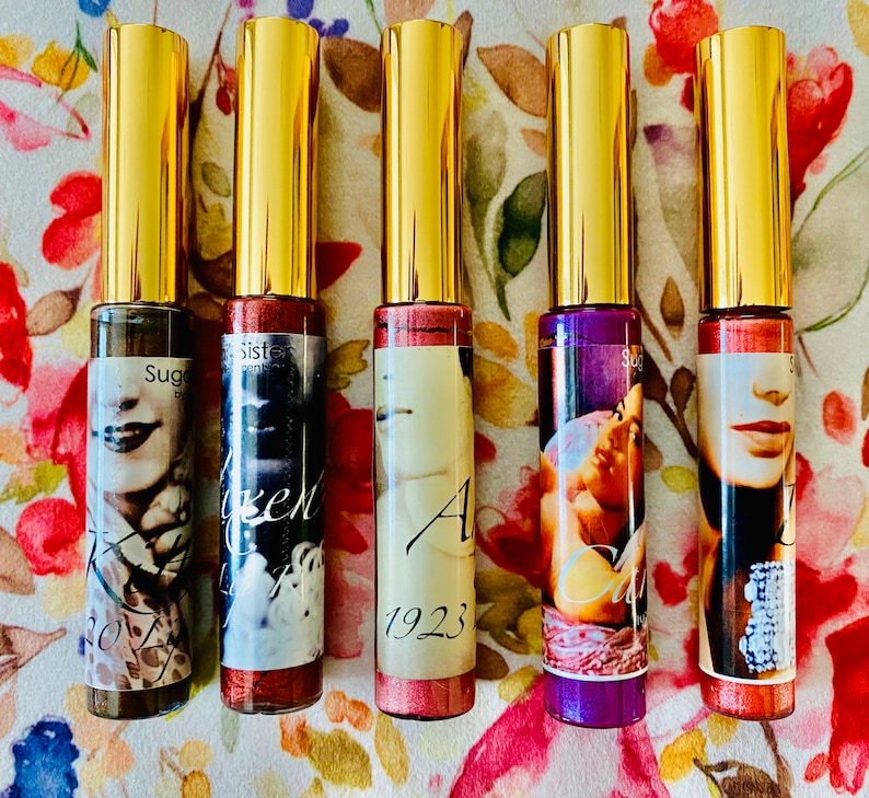 Puede incluir: Cinco peque&ntilde;os frascos de vidrio con tapas doradas y etiquetas. Las etiquetas presentan un retrato vintage de una mujer con el texto "Sugar", "Sister", "Angel 1923", "Carrie" y "Sugar".