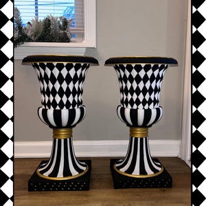 May include: Two decorative urns with black and white diamond patterns, black and white striped bases, and gold accents. The urns have a black top with gold trim and are displayed on a wooden floor. The text "@madebymicahb" is visible.