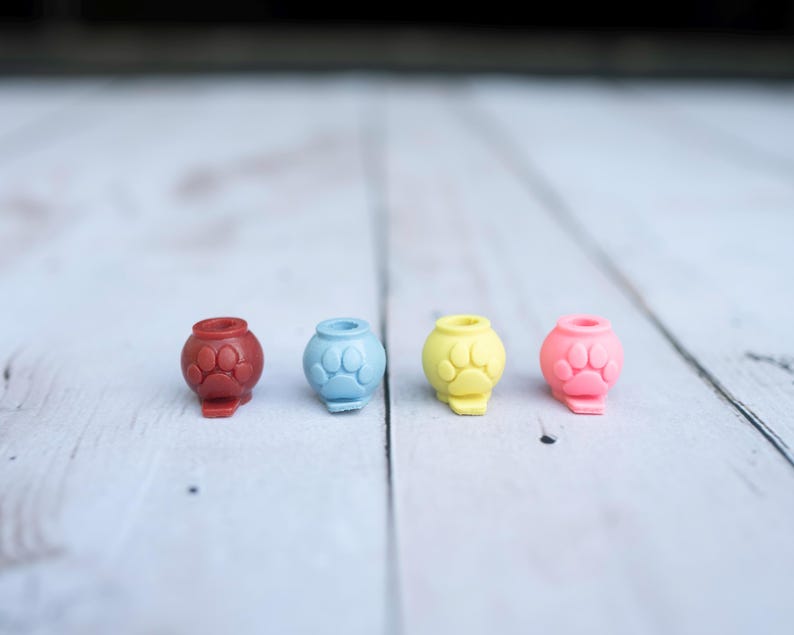 May include: Four small, spherical beads arranged in a row, each featuring a raised paw print design on the front. The beads are coloured dark red, light blue, yellow, and pink, and each has a circular opening at the top for threading purposes.