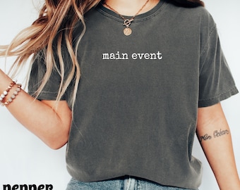 Puede incluir: Camiseta gris oscuro con las palabras "main event" impresas en blanco. La camiseta es de cuello redondo y parece estar hecha de un material suave y cómodo. La palabra "pepper" está impresa en negro en la parte inferior.