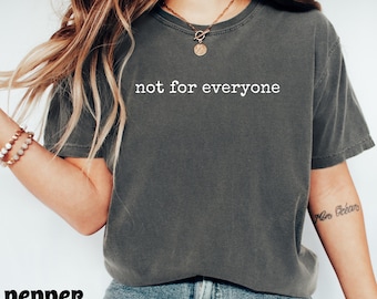 May include: A dark gray t-shirt with the text "not for everyone" in white. The shirt is a crew neck style and appears to be made of a soft, comfortable material. The word "pepper" is at the bottom left of the image.