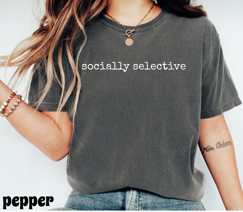 May include: A dark gray t-shirt with the words "socially selective" printed in white. The shirt is a crew neck and appears to be made of a soft material. The word "pepper" is printed in the bottom left corner.