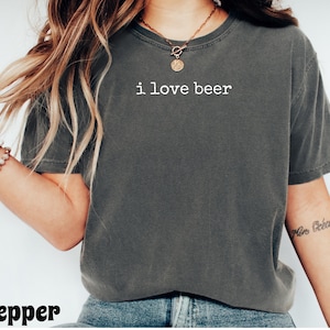 May include: A dark gray t-shirt with the text "i love beer" in white. The shirt is a casual style, likely made of cotton, and has a relaxed fit. The word "pepper" is at the bottom of the image.
