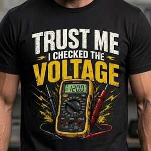 May include: Black t-shirt with the text "TRUST ME I CHECKED THE VOLTAGE" in white and yellow. The graphic features a yellow multimeter displaying 120.0, with black and red probes. The shirt is worn by a person with a beard.