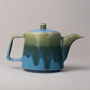 Könnte beinhalten: Eine Keramik-Teekanne mit Deckel, Henkel und Ausguss. Die Teekanne ist überwiegend blau, mit einem Farbverlauf von Grün und Braun am oberen Rand. Der Griff ist rechteckig und der Ausguss spitz.