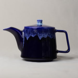 Può includere: Teiera in ceramica blu scuro con un effetto smaltato blu chiaro a goccia sul bordo e sul coperchio. Presenta un manico quadrato e un beccuccio. Il coperchio ha un piccolo pomello rotondo. Un articolo per la cucina.