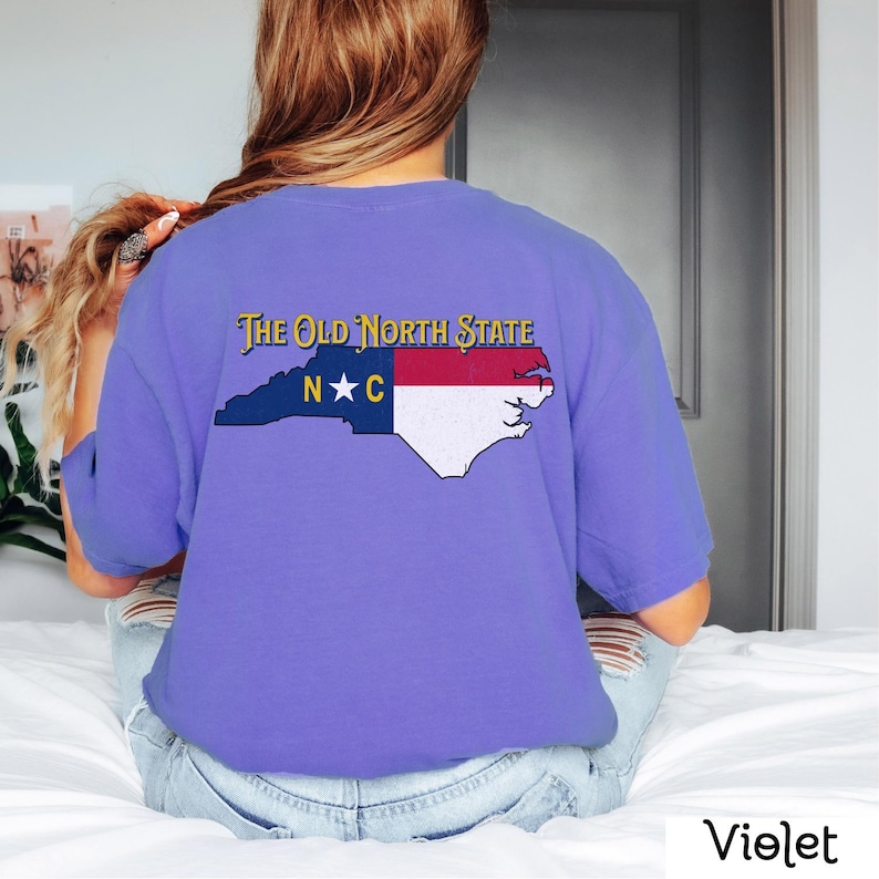 May include: A purple t-shirt with a graphic of the state of North Carolina with the words "The Old North State" and "N*C" printed on it.
