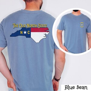 May include: A blue jean t-shirt with a vintage-style graphic of the North Carolina state flag and the text "The Old North State" on the back. The front of the shirt has a small graphic of the state flag with the letters "N.C." in a circle.