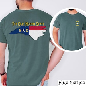 May include: A blue spruce t-shirt with a vintage-style North Carolina state outline and flag design on the back. The front of the shirt has a small, gold embroidered "NC" logo with a star.