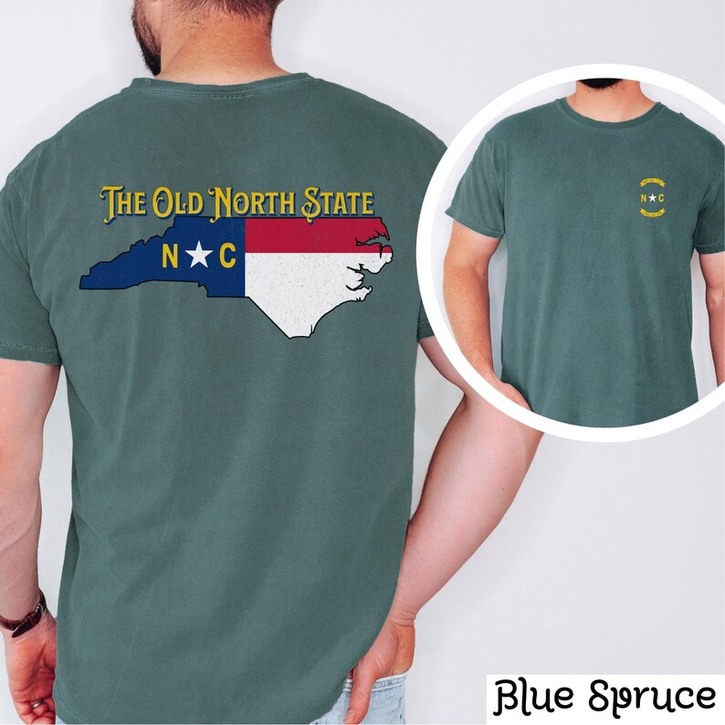 May include: A blue spruce t-shirt with a vintage-style North Carolina state outline and flag design on the back. The front of the shirt has a small, gold embroidered "NC" logo with a star.