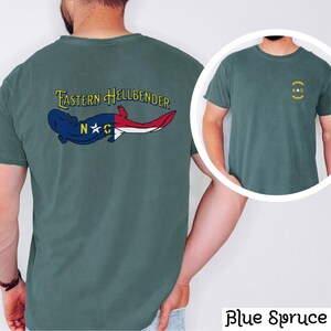 May include: A teal blue t-shirt with a graphic of a salamander with the words "Eastern Hellbender" and "N*C" on the back. The front of the shirt has a small graphic of a circle with a star and the letters "N*C" inside.