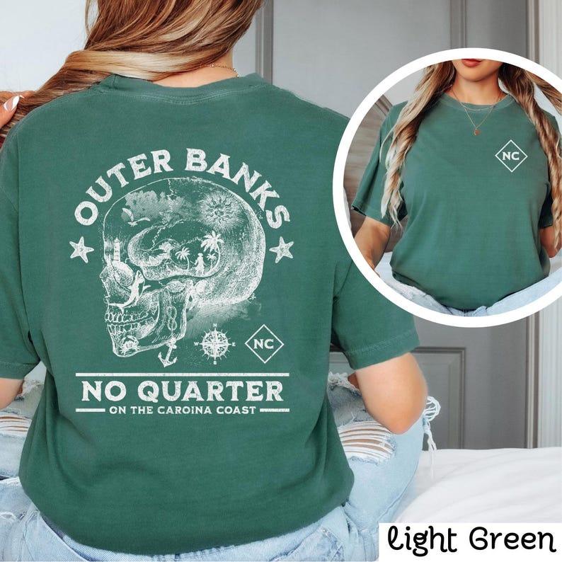 May include: A light green t-shirt with a white graphic of a skull with a compass and anchor. The text "Outer Banks" is above the skull and "No Quarter on the Carolina Coast" is below the skull.