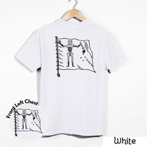 May include: White t-shirt with a black and white graphic of a skeleton holding a sword and a heart on a flag. The shirt is hanging on a wooden hanger. The words "Front Left Chest" are printed on the bottom left of the shirt.