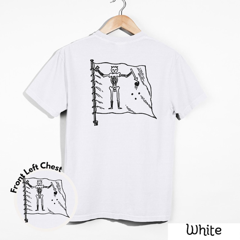 May include: White t-shirt with a black and white graphic of a skeleton holding a sword and a heart on a flag. The shirt is hanging on a wooden hanger. The words "Front Left Chest" are printed on the bottom left of the shirt.