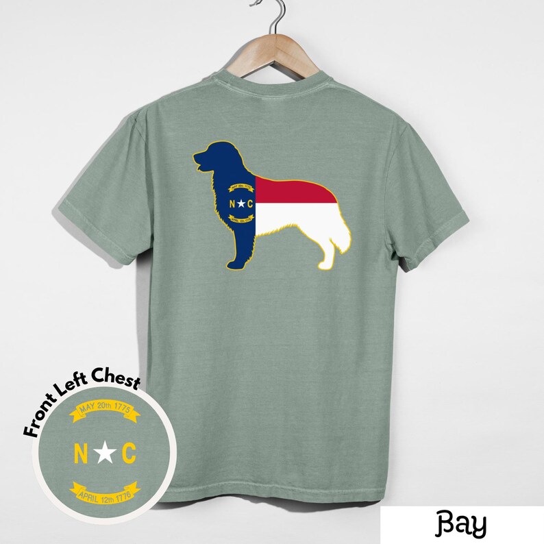 Puede incluir: Camiseta verde claro con la silueta de un perro en la espalda, que incorpora el dise&ntilde;o de la bandera del estado de Carolina del Norte. El pecho izquierdo delantero tiene un gr&aacute;fico circular con las letras "N" y "C" y las fechas "20 de mayo de 1775" y "12 de abril de 1776".