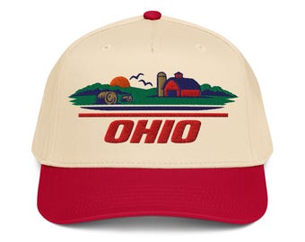 May include: A cream-colored baseball cap with a red brim and a red button on top. The front features an embroidered landscape of a red barn, green hills, a sun, and birds, with the word OHIO in bold red letters underneath the scene.
