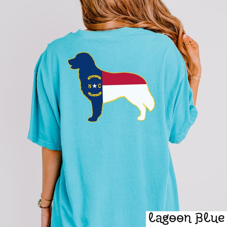 Puede incluir: Camiseta azul claro con un gr&aacute;fico de la silueta de un perro relleno con el dise&ntilde;o de la bandera del estado de Carolina del Norte. El texto "Lagoon Blue" est&aacute; impreso en la esquina inferior derecha.