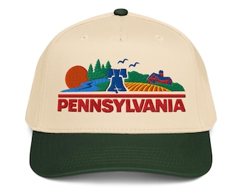 May include: A cream-colored baseball cap with a dark green brim and a dark green button on top. The front features an embroidered landscape graphic of a red sun, green trees, a blue river, a blue Liberty Bell, and a red barn, with the word PENNSYLVANIA in red.