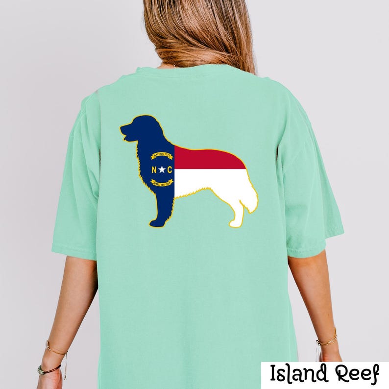 Puede incluir: Una camiseta verde claro con la silueta de un perro rellena con el dise&ntilde;o de la bandera del estado de Carolina del Norte. El contorno del perro es azul marino, con los colores de la bandera rojo, blanco y azul. El texto "Island Reef" est&aacute; en la parte inferior.