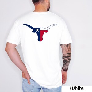 May include: White t-shirt featuring a graphic of a longhorn with the Texas flag design. The longhorn is in blue, red, and white. The shirt is a short-sleeved crew neck.