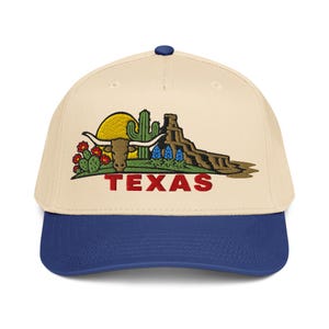 May include: A baseball cap with a cream-coloured crown and a navy blue brim. The cap features an embroidered design of a longhorn, cactus, and the word "TEXAS" in red, set against a yellow sun and desert landscape.