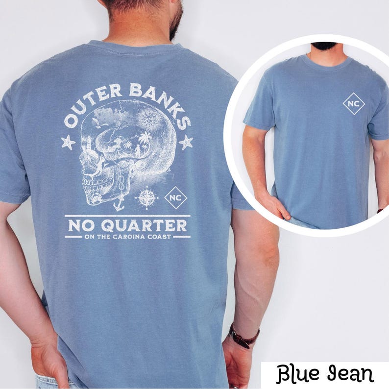 May include: A blue jean t-shirt with a white graphic on the back. The graphic features a skull with a compass and the text "Outer Banks No Quarter - On the Carolina Coast". The front of the shirt has a small white square with the letters "NC" in the center.