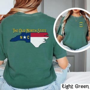 May include: A light green t-shirt with a graphic of the state of North Carolina and the text "The Old North State" and "N*C".